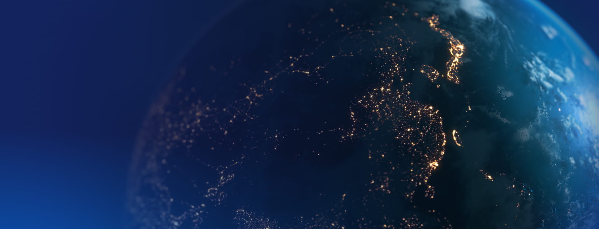 View of Earth from space at night, showing illuminated city lights across continents, deep blue oceans, cloud formations, and the planet’s curved horizon